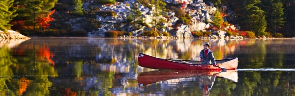 A man solo paddling a canoe on Grace Lake in autumn